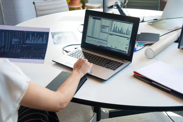Business person evaluating financial charts on a laptop in a modern office setting. Molntjänster och hosting: avtal, säkerhet och kostnad